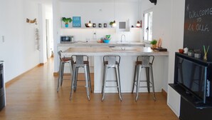 A modern kitchen with a central island, bar stools, a microwave, and a chalkboard with a welcome message. - Garza Playa - Altea, Costa Blanca (Altea)