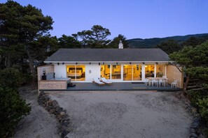 A modern house with a large deck, a bedroom with a sliding door, and a dining area.