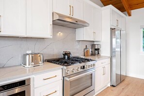 A modern kitchen with white cabinets, stainless steel appliances, and a marble countertop.