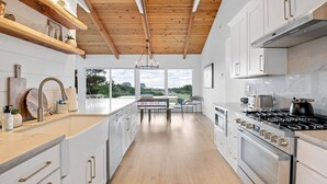 Una cocina moderna con armarios blancos, techo de madera y un ventanal con vistas a un paisaje pintoresco.