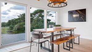 Un comedor moderno con una mesa y sillas de madera, ventanas amplias que ofrecen vistas al exterior y una lámpara colgante.
