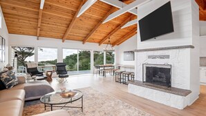 Amplia sala de estar con techo alto, chimenea y ventanas grandes que ofrecen vistas al exterior.
