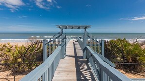 A wooden boardwalk leading to a beach with a clear view of the ocean and a blue sky. - SouthernVilla Ticket to Paradise (Palm Coast)