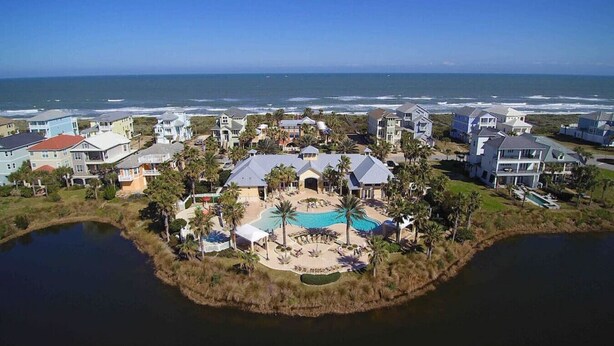 An aerial view of a coastal residential area with houses, a swimming pool, and a small island with a dock. - SouthernVilla Ticket to Paradise (Palm Coast)