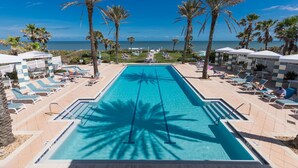 A pool area with lounge chairs and umbrellas, palm trees, and a view of the ocean. - SouthernVilla Ticket to Paradise (Palm Coast)