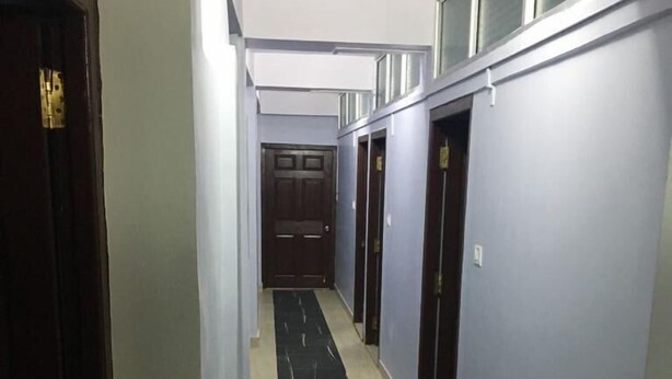 A narrow hallway with a black and white tiled floor, light blue walls, and a wooden door at the end. - Emerald Homes (Port Blair)