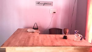 A reception desk with a sign labeled "Reception" on the wall, a telephone, a small decorative item, and a chair. - Emerald Homes (Port Blair)