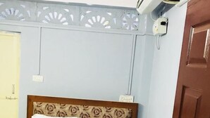 A neatly made bed with white sheets and a beige blanket, a wooden headboard with a patterned design, and a wall-mounted air conditioning unit. - Emerald Homes (Port Blair)
