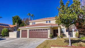 A two-story house with a red-tiled roof, a garage, and a well-maintained lawn. - Lux Haven with Movie Theater, Hot Tub, Office, and Grill NestNights (Santa Clarita)