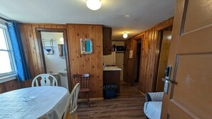 Una habitación acogedora con suelo de madera, una mesa de comedor con sillas, una cama y una pequeña cocina en el fondo.