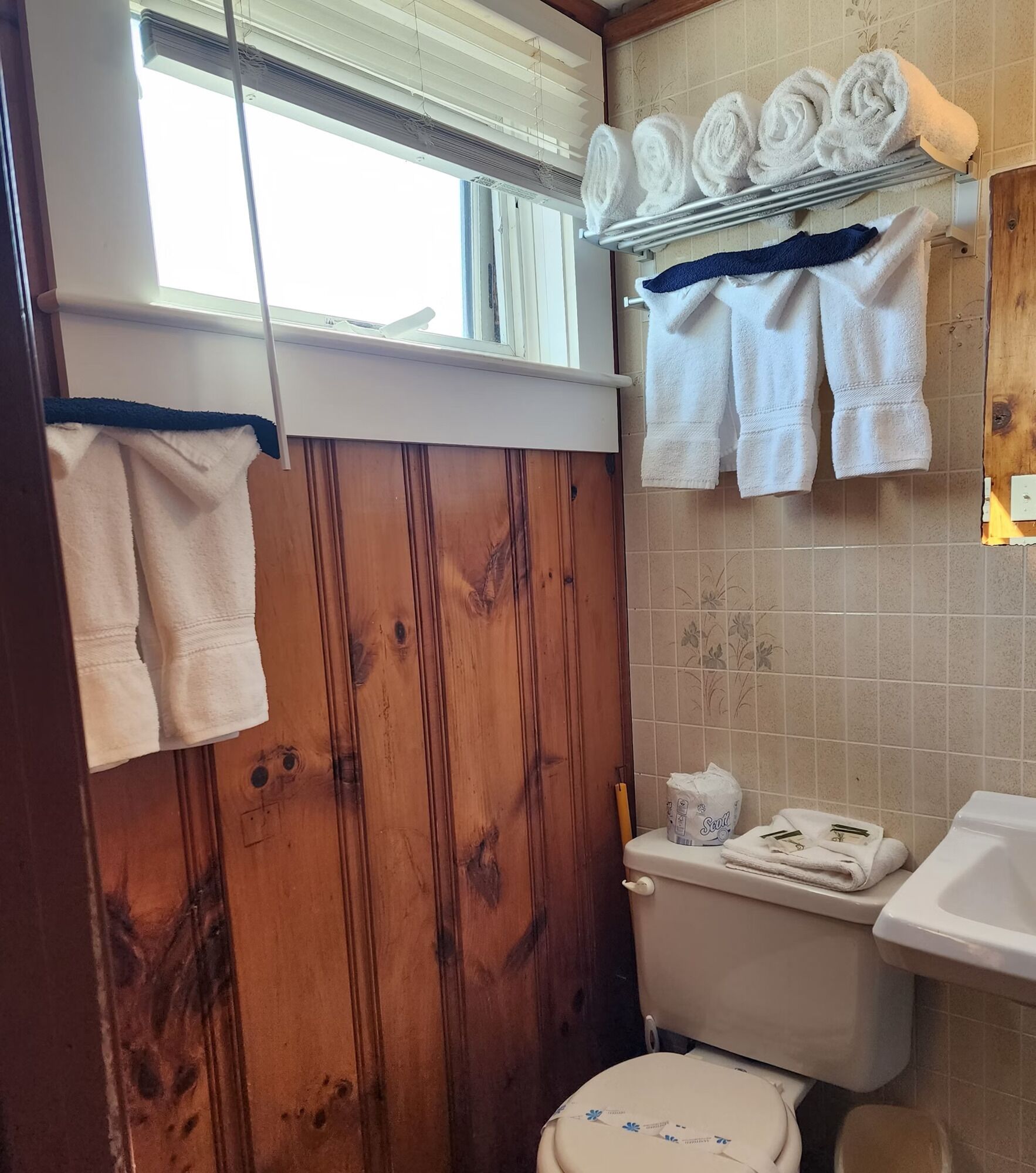 Ein Badezimmer mit Holzwänden, einer Toilette, einem Waschbecken und Handtüchern an einem Ablagefach.