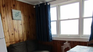 Una habitación con pared de madera, un sofá, una mesa de comedor con sillas y una ventana con cortinas.