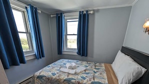 Un dormitorio con cama, cómoda, ventana con cortinas y una lámpara en el techo.