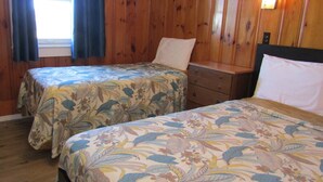A room with two beds, wooden walls, a window with curtains, and a nightstand with a lamp. - Unwind on the Oceanside in the BlueFish Saturday Cottage at Oceana Cottages (North Truro)