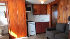 A compact kitchen with wooden cabinets, a stove, and a sink. - Unwind on the Oceanside in the BlueFish Saturday Cottage at Oceana Cottages (North Truro)