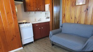 A compact kitchen with wooden cabinets, a white stove, and a gray sofa. - Unwind on the Oceanside in the BlueFish Saturday Cottage at Oceana Cottages (North Truro)