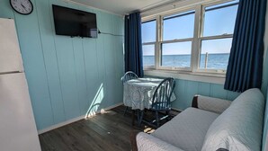 A compact room with a bed, a small table, a chair, a TV, and a window with curtains.