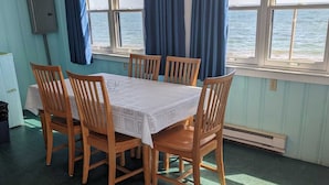 A dining area with a table and chairs, large windows with curtains, a view of the sea, and a tiled floor. - Tranquil Getaway at the Dolphin Sunday cottage located at the Oceana Cottages (North Truro)