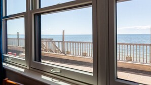 A view from a window overlooking a wooden deck and the sea. - Tranquil Getaway at the Dolphin Sunday cottage located at the Oceana Cottages (North Truro)
