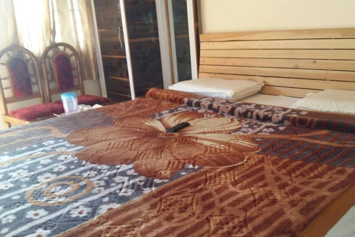 A bed with a patterned bedspread, a wooden headboard, and a window with curtains.