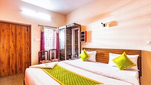 A hotel room with a wooden door, a bed with white linens and green accents, a wooden headboard, and a window with a curtain. - SV Residency (Ootacamund)