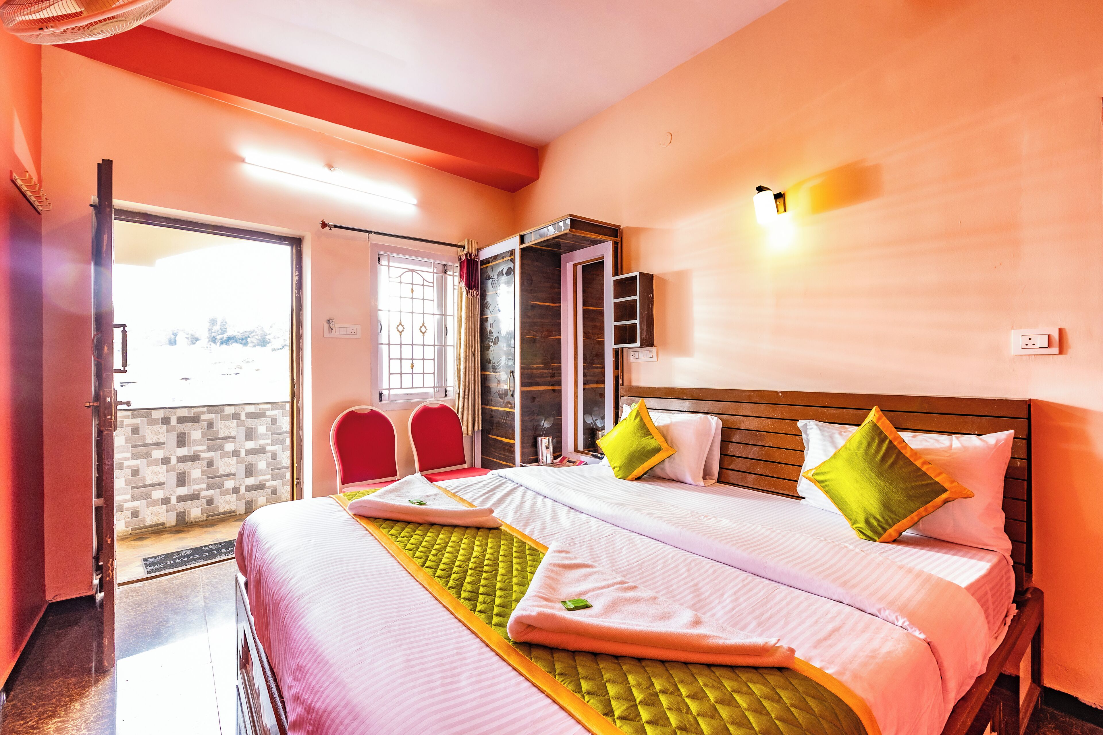 Een hotelkamer met een bed, twee stoelen, een kledingkast en een deur naar buiten.