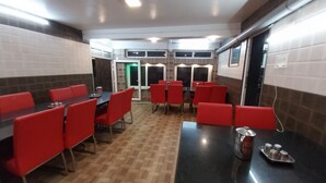 A restaurant with red chairs and black tables, a tiled floor, and a counter with condiments. - SV Residency (Ootacamund)