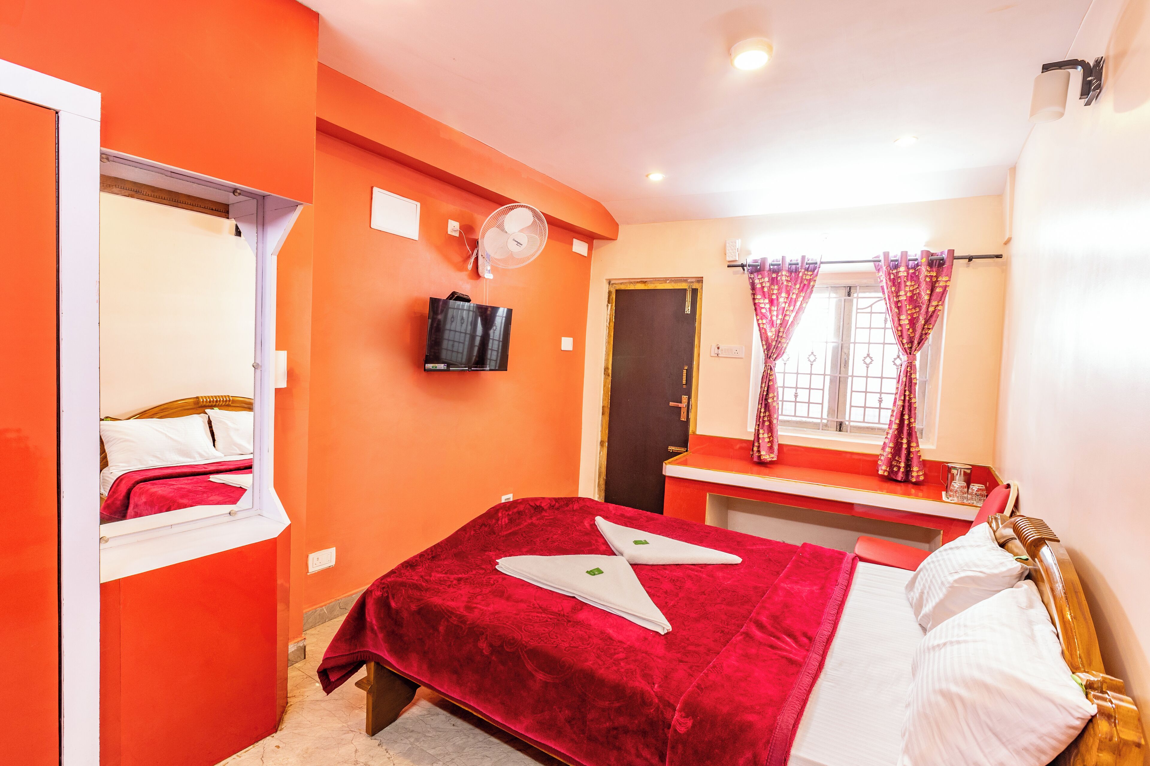 Un dormitorio con cama, escritorio, silla, televisión y ventana con cortinas.