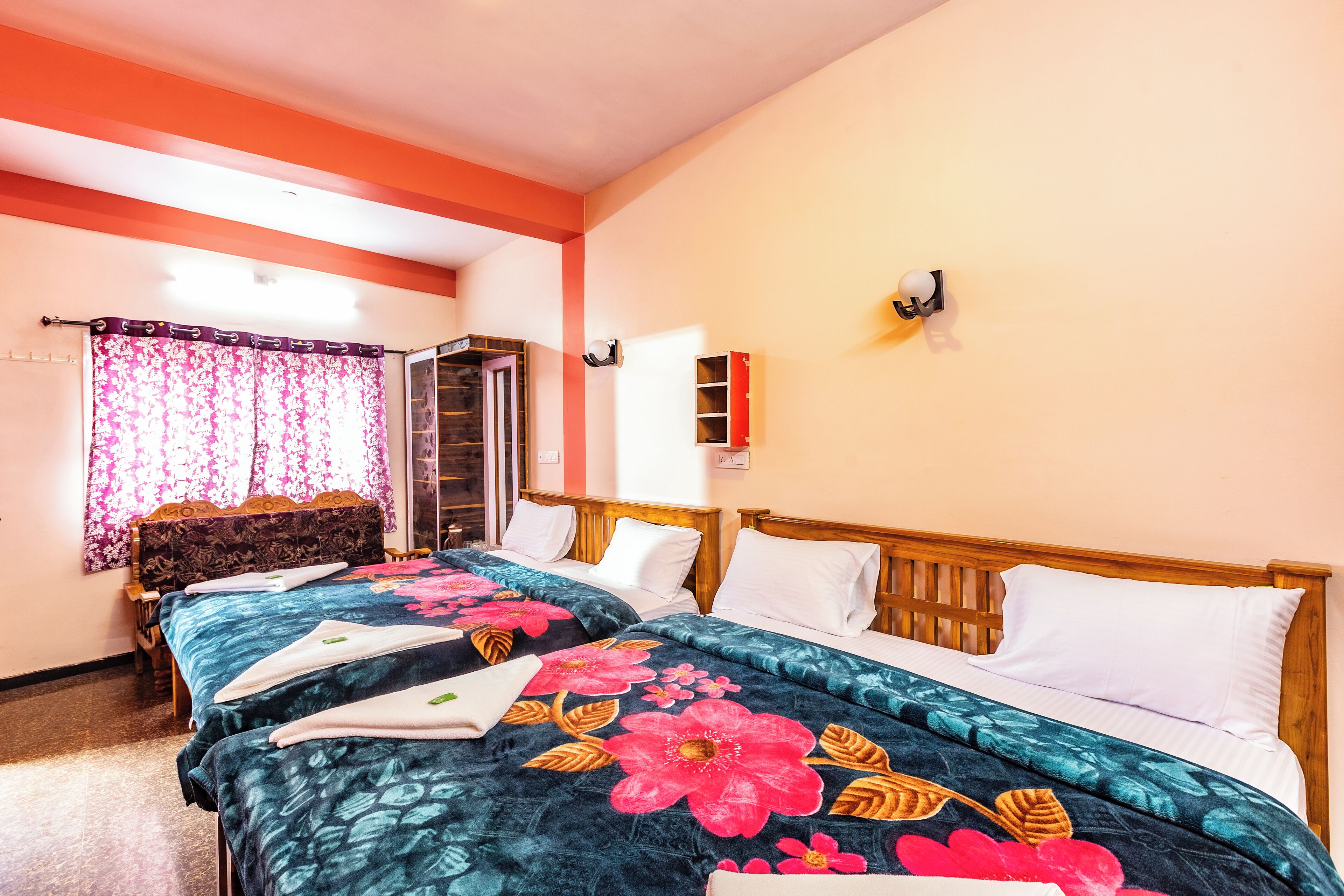 Camera d'albergo con due letti, una testiera in legno, una finestra con tende rosa e una mensola a parete.