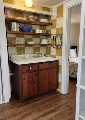 Compact kitchen area with a sink, shelves, and a door leading to another room.