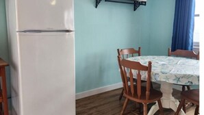 Una habitación con un refrigerador blanco, sillas de madera, una mesa con mantel floral y una pared azul.