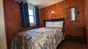 Une chambre avec des lambris en bois, un lit avec une literie à motifs floraux, une table de chevet et un miroir.