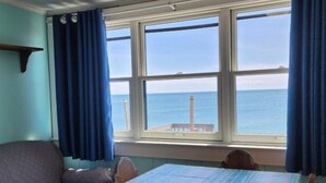 Une chambre avec un lit, une table et une vue sur la mer, grâce à de grandes fenêtres.