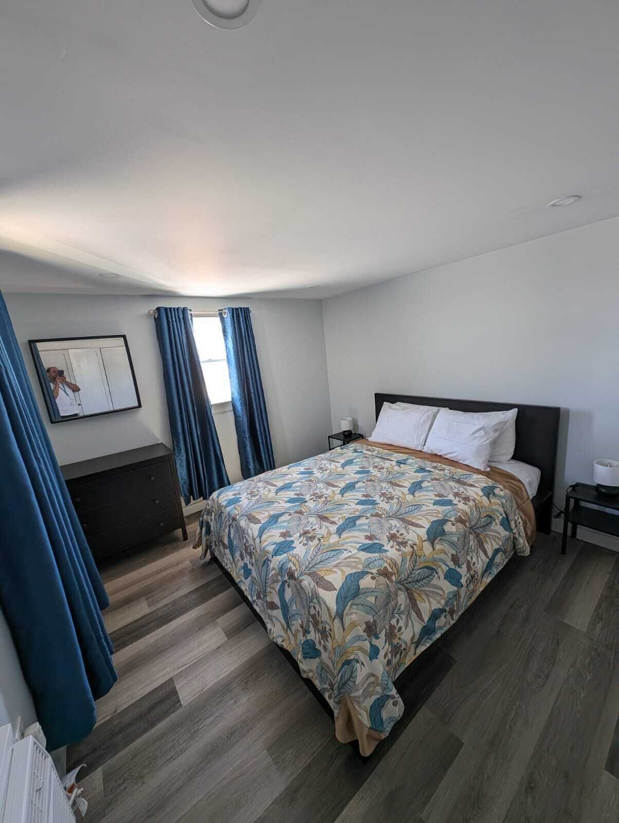 Quarto com cama, penteadeira, mesa de cabeceira e janela com cortinas.