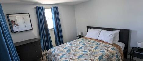 Quarto com cama, penteadeira, mesa de cabeceira e janela com cortinas.