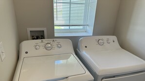 Two front-loading white washers with control panels, a window with blinds, and a light switch on the wall.