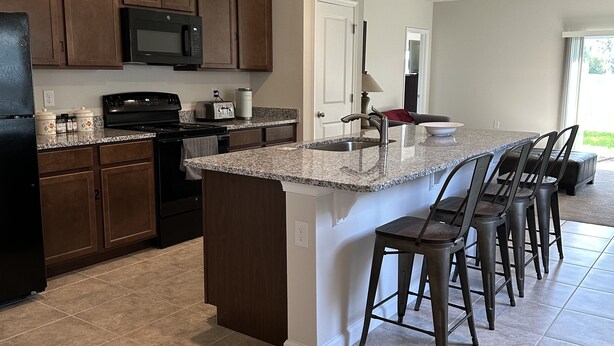 A modern kitchen with a central island, dark wooden cabinets, a black refrigerator, and a microwave.