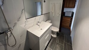Ett modernt badrum med en tvättställsskiva i marmor, en dusch, en toalett och en spegel.