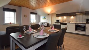 A modern kitchen with a wooden ceiling, a dining area with a table set for four, and a view of the living room. - Comfortable apartment in Burg-Reuland with shared terrace (Burg-Reuland)