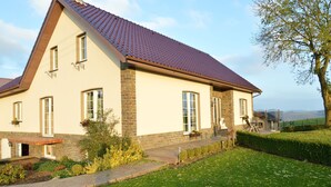A two-story house with a red-tiled roof, brick and stucco exterior, and a well-maintained garden. - Comfortable apartment in Burg-Reuland with shared terrace (Burg-Reuland)