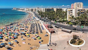 A beach with numerous umbrellas and people, a road parallel to the beach, and buildings in the background. - Comfortable spacious family house with large terrace and garden Beach & Bars (Torrevieja)
