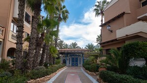 A pathway leading to a building with a blue door, surrounded by palm trees and a tiled walkway. - Comfortable spacious family house with large terrace and garden Beach & Bars (Torrevieja)