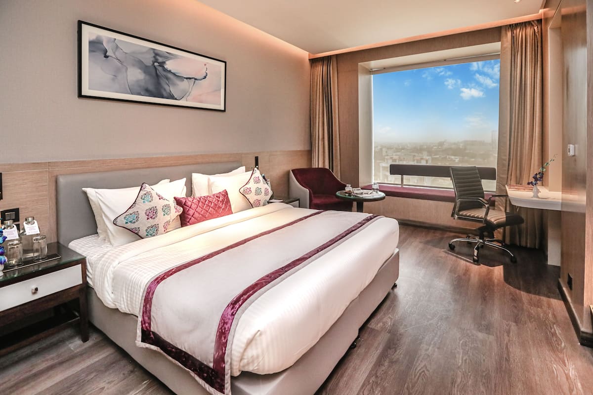 A hotel room with a large bed, a desk, a chair, and a view of the city.
