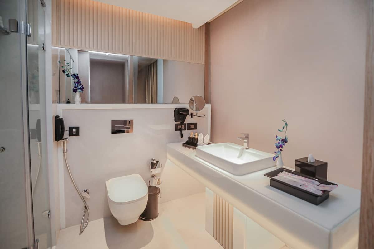 A modern bathroom with a large mirror, a white sink, a toilet, and a shower.