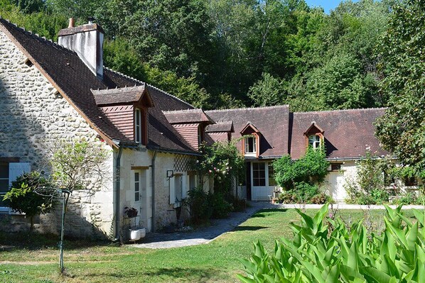 A stone building with a sloped roof, a small garden, and a pathway leading to a door.