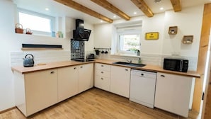 A modern kitchen with wooden beams, white cabinetry, a built-in microwave, and a dishwasher. - Charming renovated gîte (Rimbach-prés-Guebwiller)