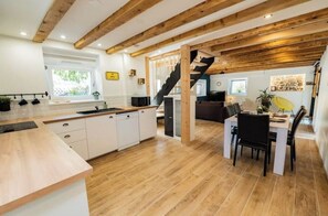 A modern kitchen with wooden beams, a dining area with a black chair, and a staircase leading to another level. - Charming, renovated vacation home (Rimbach-prés-Guebwiller)