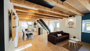 A spacious living area with a staircase leading to a kitchen, wooden beams on the ceiling, and a dining area with a table and chairs. - Charming renovated gîte (Rimbach-prés-Guebwiller)