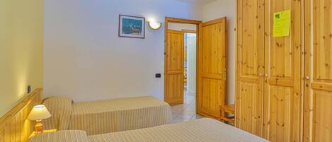 Una habitación con dos camas, un armario de madera y una mesita con lámpara.