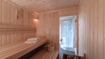 A sauna room with wooden benches, a wooden bucket, and a glass door leading to a shower area.